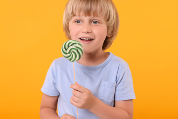 Wall Mural - Happy little boy with lollipop swirl on orange background