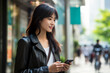 © Surachetsh - An attractive and beautiful Asian woman is using a mobile phone to text message and call someone while walking through a busy and crowded city. Generative AI.