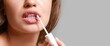 © Pixel-Shot - Beautiful woman applying lipstick against grey background with space for text, closeup