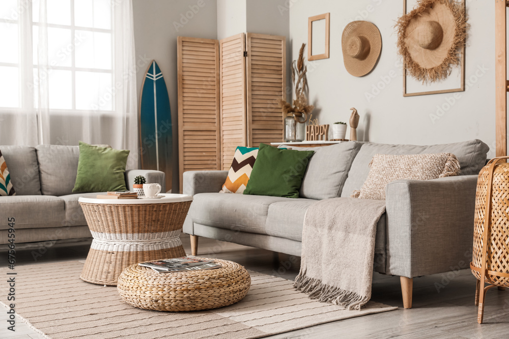 Interior of light living room with surfboard, table and sofas