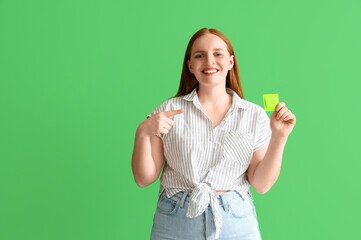 Wall Mural - Young woman pointing at condom on green background