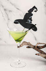 Sticker - Glass of delicious cocktail for Halloween with paper hat and wood on light background, closeup