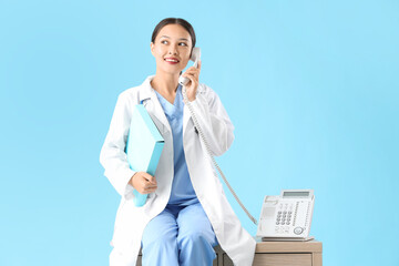 Sticker - female asian doctor talking by telephone on blue background