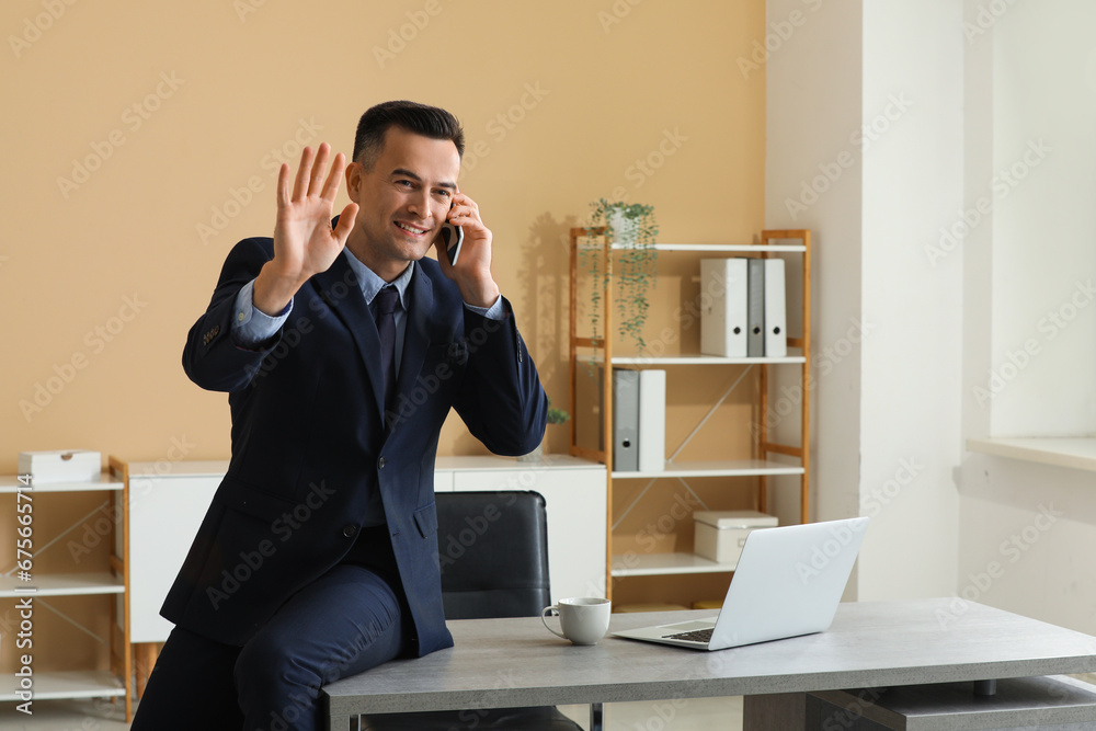 Handsome businessman with mobile phone waving hand in office