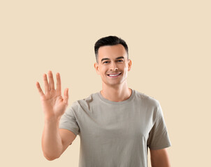 Poster - Young man waving hand on beige background