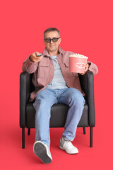 Poster - Mature man with 3D glasses and popcorn watching TV in armchair on red background