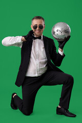 Wall Mural - Cool mature man in suit with disco ball on green background