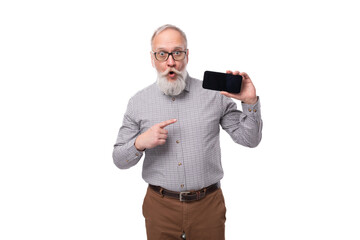 Wall Mural - modern smart gray-haired mature businessman with a beard and mustache in a shirt and trousers holds a smartphone screen forward