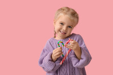 Cute Little Girl With Tasty Candy Canes On Pink Background