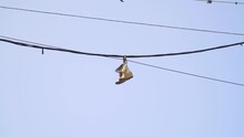 Shoes Hanging By Laces From A Wire. Pairs Of Shoes Are Hanging On Electric Wires Against The Sky. Old Sneakers Hanging On Wires As A Symbol Of Drug Trafficking In This Area Of The City.