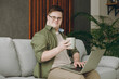 © ViDi Studio - Young IT man with down syndrome wear casual clothes work hold use laptop pc computer sits on grey sofa couch stay at home flat rest spend free time in living room. Genetic disease world day concept.