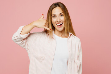 Young smiling fun happy woman she wear shirt white t-shirt casual clothes doing phone gesture like says call me back isolated on plain pastel light pink background studio portrait. Lifestyle concept.