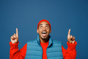 Sticker - Young smiling man of African American ethnicity wear padded vest red hat point index finger aside on area mock up isolated on plain dark royal navy blue background studio portrait. Lifestyle concept.