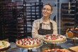 © ViDi Studio - Young happy seller consultant woman wearing uniform working at supermaket store grocery shop standing near sweet pastry bakery products selling inside hypermarket. Purchasing food gastronomy concept.