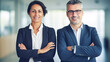 © BlazingDesigns - Portrait of smiling mature businessman and young business woman standing arms crossed in office. Two diverse colleagues planning and collaboration.