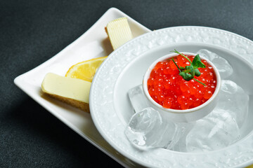 Wall Mural - A bowl of red caviar on ice, served with toasted bread. Appetizer. On a dark stone background. Free space for text.