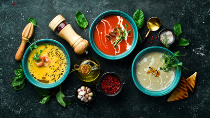 Wall Mural - A set of colored soups. Tomato soup, pumpkin and mushroom soup. In a blue plate. On a black stone background.