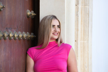 Young and beautiful blonde woman with overweight is leaning on the wall and dressed in casual and modern clothes. The woman stares at the camera with an expressionless face.