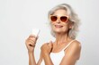 Senior beautiful woman with sunglasses holds sun protection cream. Elderly woman posing with sunblock product tube. Generate ai