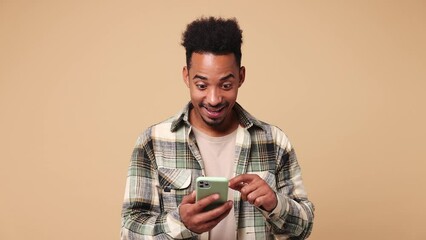 Wall Mural - Happy joyful young man of African American ethnicity he wear shirt casual clothes hold use point finger on mobile cell phone just found out great big win news isolated on plain beige brown background