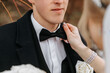 Cropped wedding portrait of the groom. The bride fixes the groom's bow tie. A man in a black suit. Winter wedding