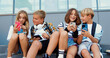 © serg - Cheerful stylish group of school children sitting on bench outdoors using and mobile phone communicating online. Friendship, technology concept. Playing game online