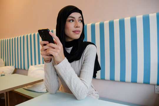Young woman in hijab using phone in cafe