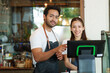 Multiracial man businessman small business cafe owner pointing at cash register with Asian girlfriend both looking camera Inside the coffee shop Behind there coffee machine in minimalist style shop