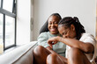 © Cultura Creative - Lesbian couple laughing while sitting on sofa at home