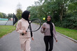Two women in hijabs walking in park with tennis racket and ball