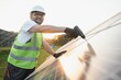 © Serhii - Portrait of smiling confident engineer technician with electrical screwdriver, standing in front of unfinished high exterior solar panel photo voltaic system