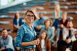 © Drazen - Female business seminar coach at convention center looking at camera.