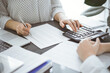 © rogerphoto - Woman accountant using a calculator and laptop computer while counting taxes with a client or a colleague. Business audit team, finance advisor