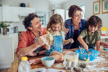 Young Family With Small Children Baking Together In Kitchen Having Fun