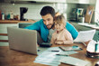 © Geber86 - Young man holding document looking at laptop with daughter at home