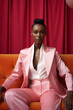 © IgnacioJulian - young black woman wearing a pink jacket and white pants sits on the couch, studio portraiture