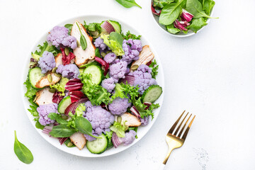 Healthy fresh salad from purple cauliflower, grilled chicken breast, cucumbers, red onion, radicchio, spinach with pumpkin seeds, white table background, top view