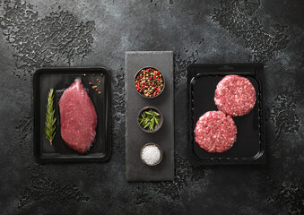 Wall Mural - Raw fresh organic beef sirloin fillet steak and mince burgers sealed in vacuum tray with  on black background with spices.