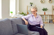 © Studio Romantic - Happy beautiful middle aged business woman with short hair, in glasses sitting with laptop computer on sofa at home, having video call meeting, looking at screen, holding pen and notebook and smiling
