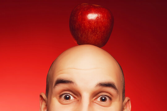 Super Idea concept. Portrait of a funny scared and confused man with fearful glance posing over red background with red apple on head. Close up. Text space. Studio shot