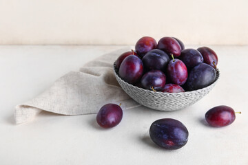 Wicker bowl with fresh ripe plums on white background