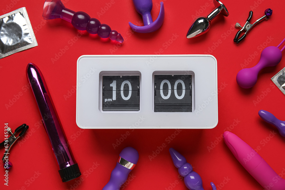 Alarm clock with different toys on red background. Time for sex