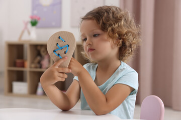 Poster - Motor skills development. Little girl playing with wooden lacing toy at table indoors