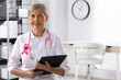 Doctor with stethoscope, clipboard and pink ribbon indoors, space for text. Breast cancer awareness