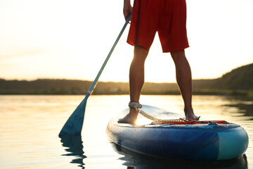 Wall Mural - Man paddle boarding on SUP board in river at sunset, closeup