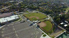 Dolly In Aerial Drone Wide Shot Approaching Empty Baseball Diamond Fields From Above Behind An American High School Surrounded By Colorful Trees And Houses On A Sunny Fall Day In Utah