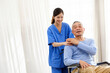 © artitwpd - The caregiver therapist stands with an Asian senior sitting in a wheelchair and touches their hands on senior shoulder together. The nursing home facilitates a support group. Image with copy space