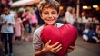 A young boy holding a large, heart shaped soft toy he won as a prize at the fun fair.
