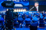 Fototapeta  - Video camera capturing global business conference in illuminated blue auditorium at export forum