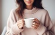 Closeup of female hands with a mug of beverage. Beautiful girl in purple sweater holding cup of tea or coffee in the morning sunlight. Mug for your design. Empty.